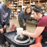 two women look on as a third throws a pot